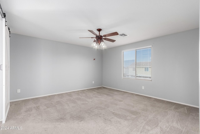 carpeted spare room featuring a barn door and ceiling fan