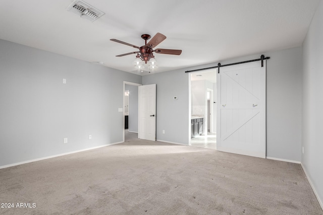 carpeted spare room with a barn door and ceiling fan