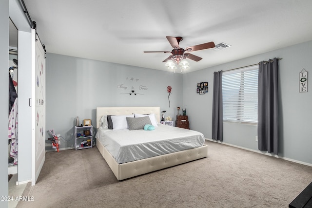 carpeted bedroom featuring a barn door and ceiling fan