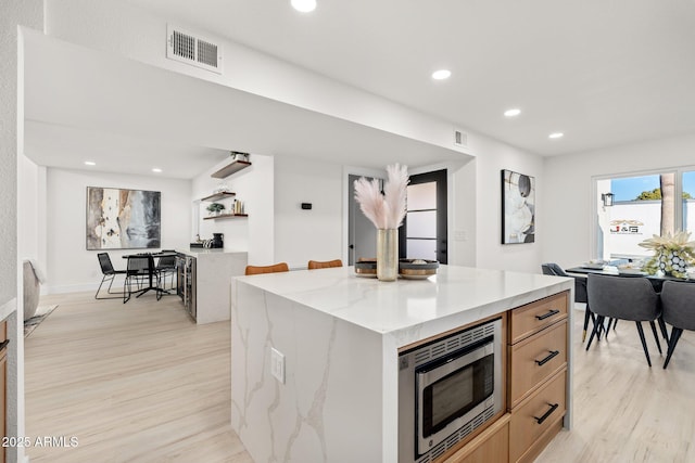 kitchen featuring a center island, stainless steel microwave, light brown cabinets, light wood-type flooring, and light stone counters