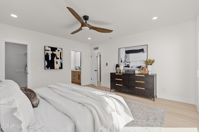 bedroom with ceiling fan, sink, ensuite bathroom, light hardwood / wood-style floors, and a walk in closet