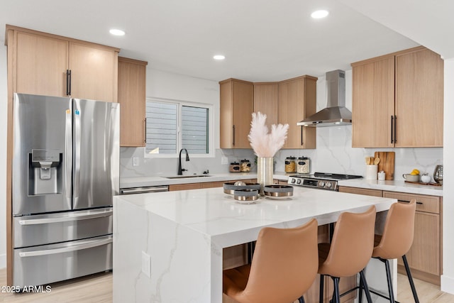 kitchen featuring a center island, wall chimney range hood, sink, light hardwood / wood-style flooring, and stainless steel appliances