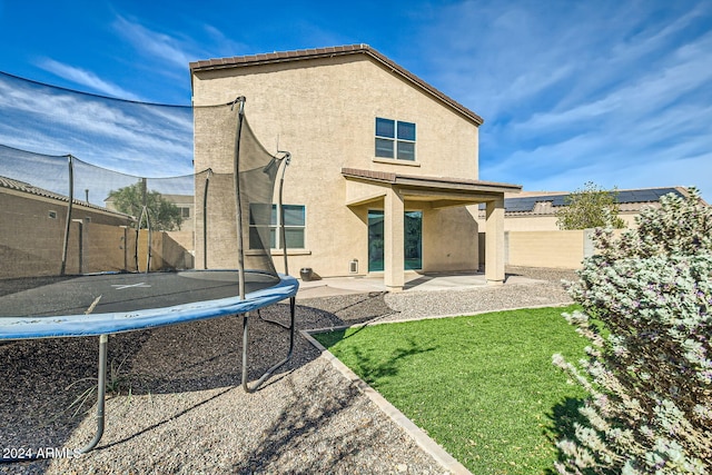 back of house featuring a lawn, a patio area, and a trampoline