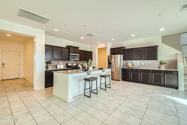 kitchen with a breakfast bar area, decorative backsplash, a center island with sink, and appliances with stainless steel finishes