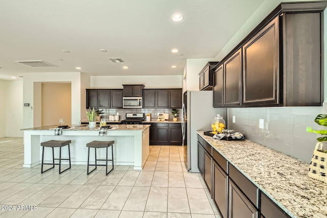 kitchen with backsplash, dark brown cabinetry, light stone countertops, and stainless steel appliances