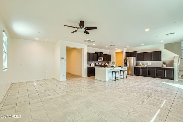 kitchen featuring a kitchen bar, decorative backsplash, stainless steel appliances, a kitchen island with sink, and ceiling fan