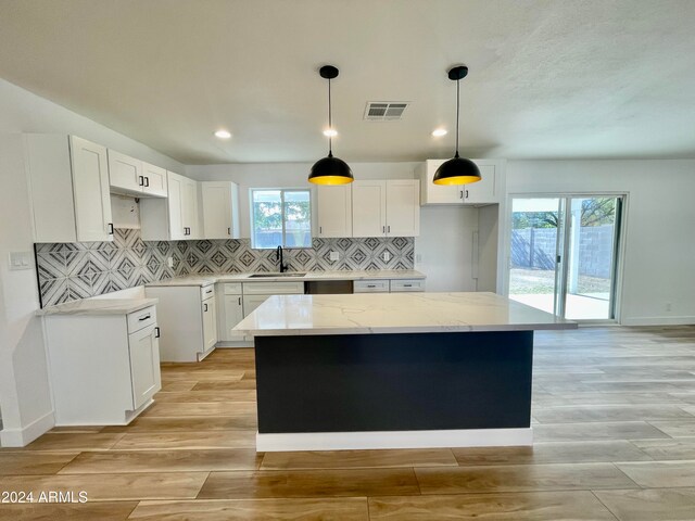 kitchen featuring white cabinetry, a kitchen island, light stone counters, and light wood-type flooring