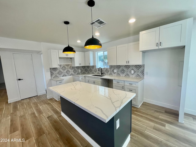 kitchen with light stone countertops, a center island, sink, light hardwood / wood-style flooring, and white cabinets