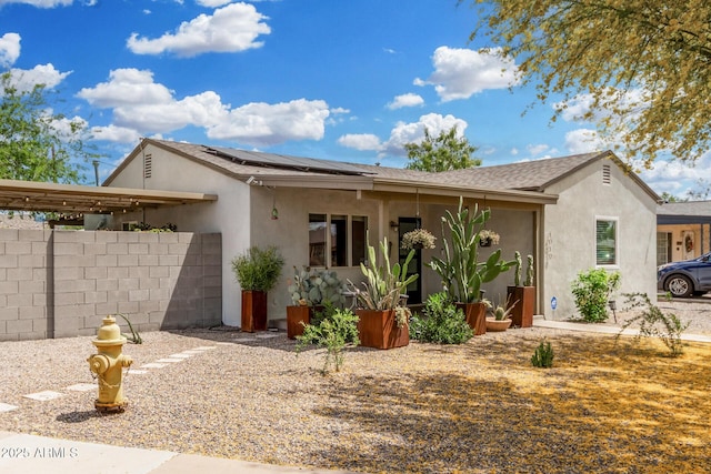view of front of property featuring roof mounted solar panels, stucco siding, and fence