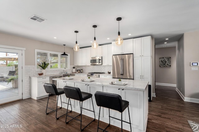 kitchen with a center island, decorative backsplash, visible vents, appliances with stainless steel finishes, and dark wood-style floors