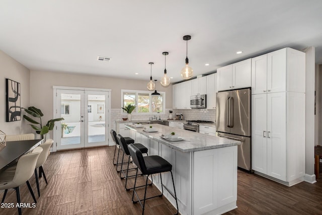 kitchen featuring tasteful backsplash, premium appliances, white cabinets, visible vents, and a kitchen island