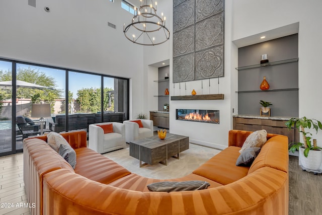 living room featuring a high ceiling, a chandelier, built in features, and light wood-type flooring