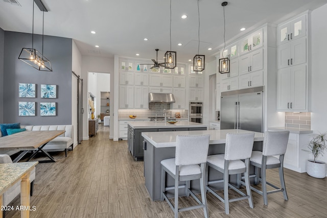 kitchen featuring appliances with stainless steel finishes, a barn door, a center island with sink, and white cabinets