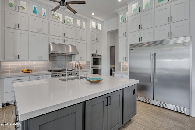 kitchen featuring white cabinetry, appliances with stainless steel finishes, light stone countertops, a kitchen island with sink, and backsplash