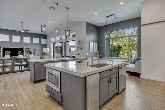 kitchen with gray cabinets, pendant lighting, stainless steel microwave, an island with sink, and sink