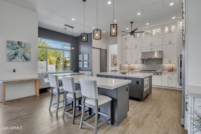 kitchen featuring decorative light fixtures, white cabinets, stainless steel gas cooktop, a barn door, and a center island with sink