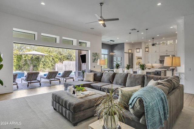 living room featuring a towering ceiling, ceiling fan, and light wood-type flooring