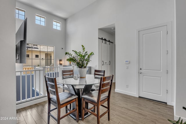 dining room with light hardwood / wood-style floors, a barn door, and a high ceiling