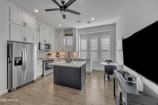 kitchen with a kitchen island, appliances with stainless steel finishes, white cabinetry, sink, and light hardwood / wood-style floors