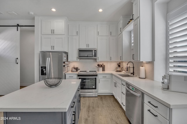 kitchen featuring sink, a kitchen island, stainless steel appliances, a barn door, and white cabinets