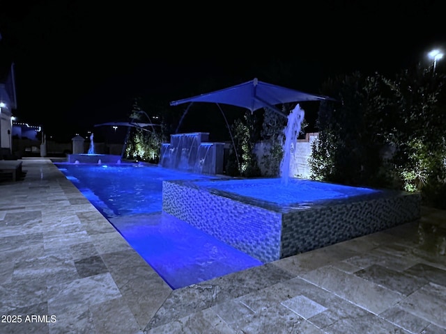 pool at night featuring pool water feature and a patio