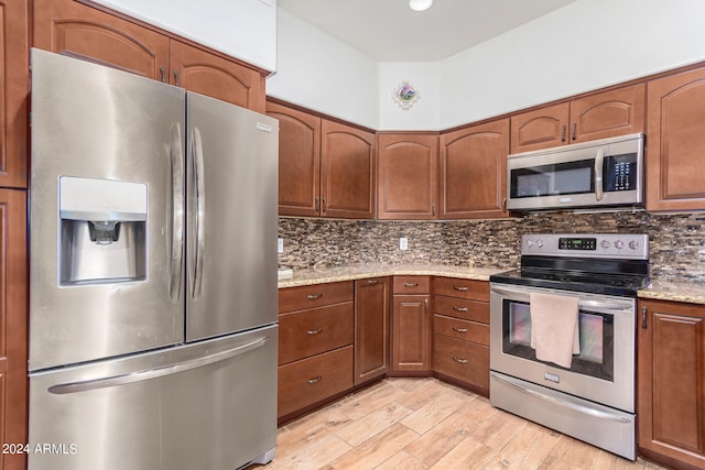 kitchen featuring light stone countertops, stainless steel appliances, backsplash, and light hardwood / wood-style flooring