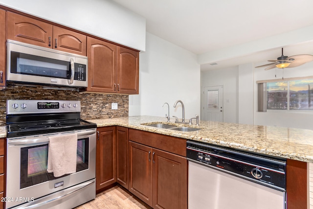 kitchen with light wood-type flooring, light stone counters, stainless steel appliances, tasteful backsplash, and sink