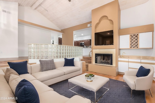 living room featuring beamed ceiling, sink, light hardwood / wood-style flooring, high vaulted ceiling, and a large fireplace