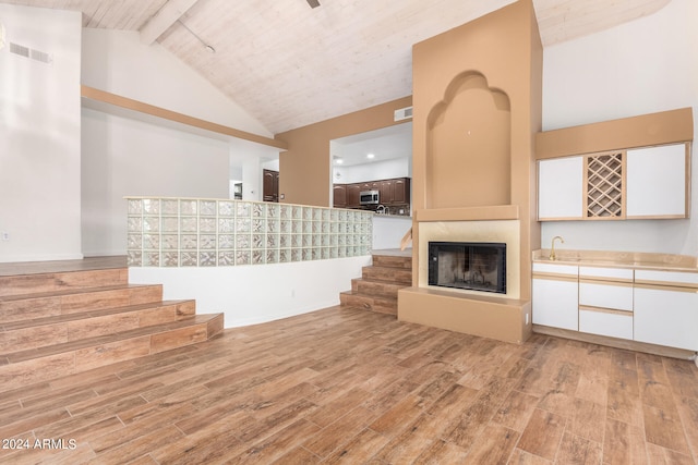 unfurnished living room with light wood-type flooring, beamed ceiling, a large fireplace, and sink