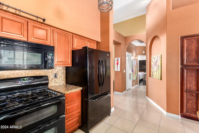 kitchen featuring light tile patterned flooring, tasteful backsplash, black appliances, light stone countertops, and a high ceiling