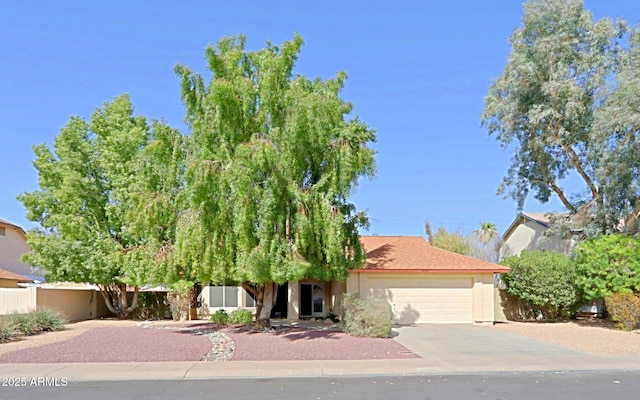 obstructed view of property featuring driveway, a garage, fence, and stucco siding