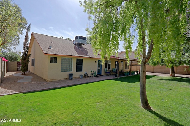 rear view of house with a lawn, a fenced backyard, roof with shingles, a patio area, and stucco siding