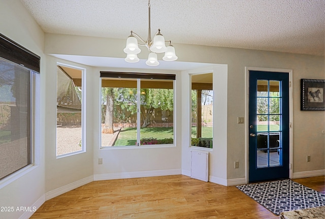 doorway to outside featuring an inviting chandelier, a textured ceiling, and wood finished floors