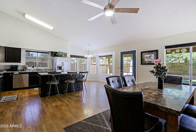 dining area featuring ceiling fan with notable chandelier, vaulted ceiling, a textured ceiling, and wood finished floors