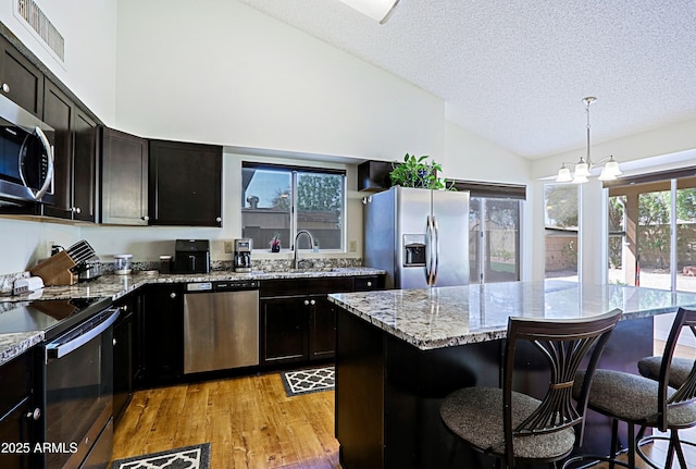 kitchen featuring a breakfast bar area, stainless steel appliances, visible vents, a sink, and light stone countertops