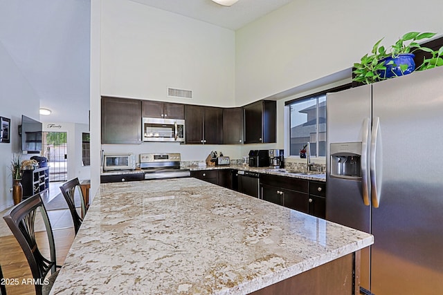 kitchen featuring stainless steel appliances, a sink, a towering ceiling, visible vents, and a center island