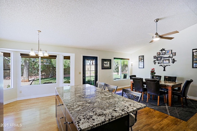 kitchen with a center island, hanging light fixtures, vaulted ceiling, light stone countertops, and light wood-type flooring