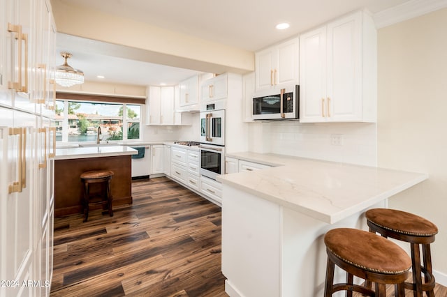 kitchen with white cabinets, kitchen peninsula, dark wood-type flooring, stainless steel appliances, and a breakfast bar area