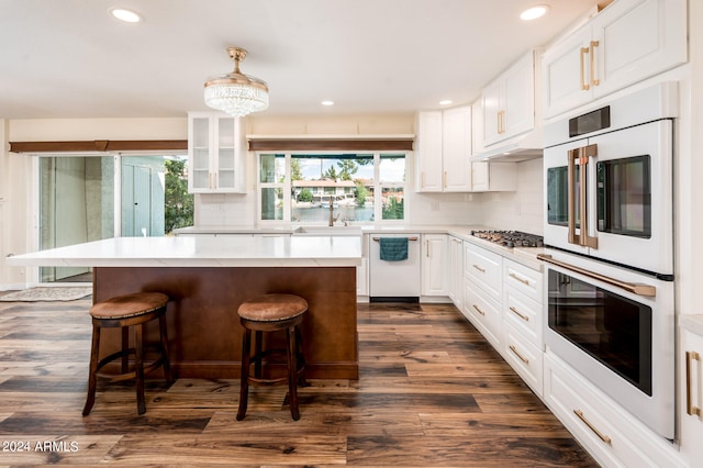 kitchen featuring white cabinets, white appliances, a kitchen island, dark wood-type flooring, and a kitchen bar