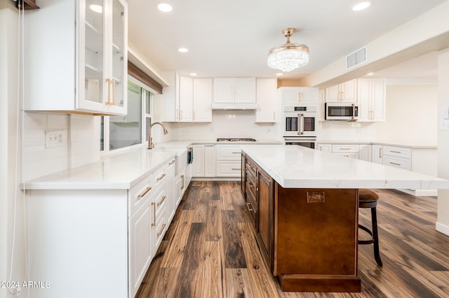 kitchen with white cabinets, a kitchen island, dark wood-type flooring, white double oven, and a kitchen bar