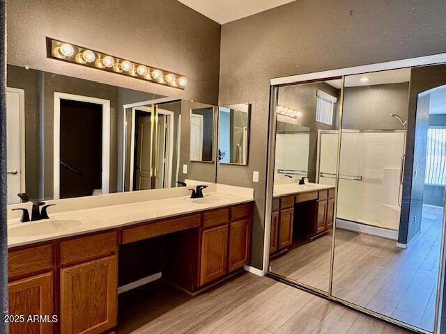 full bath featuring double vanity, a walk in shower, a sink, and wood finished floors