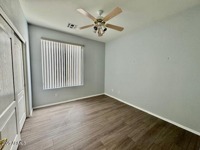 empty room with visible vents, ceiling fan, baseboards, and wood finished floors