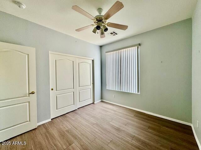 unfurnished bedroom with baseboards, a closet, visible vents, and wood finished floors