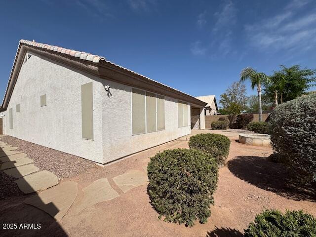 view of side of home featuring a tiled roof, fence, and stucco siding