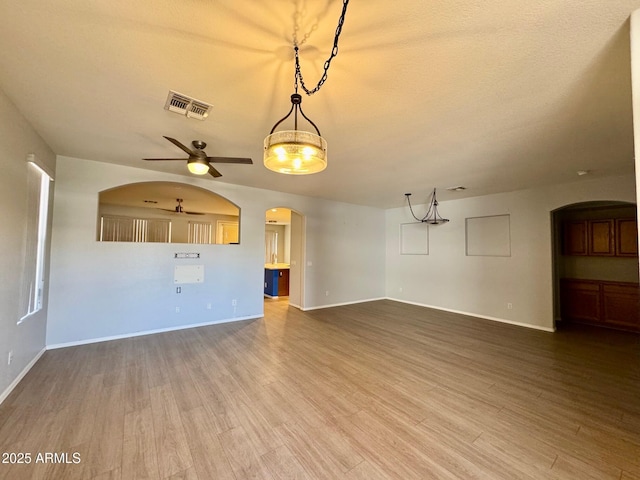 unfurnished living room with arched walkways, wood finished floors, visible vents, baseboards, and a ceiling fan