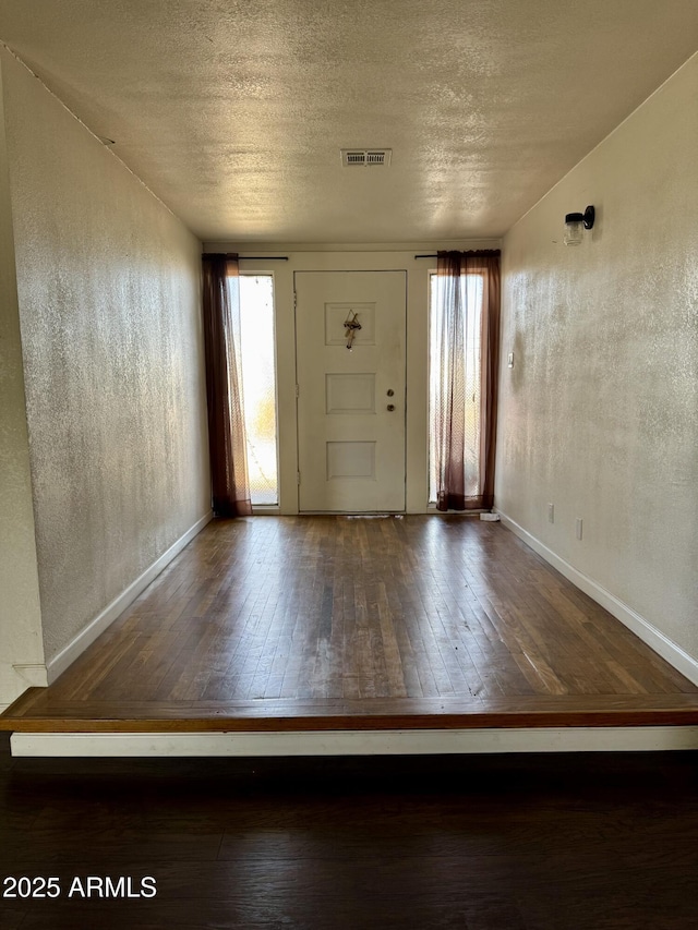 foyer entrance with a textured ceiling, a textured wall, wood-type flooring, and visible vents