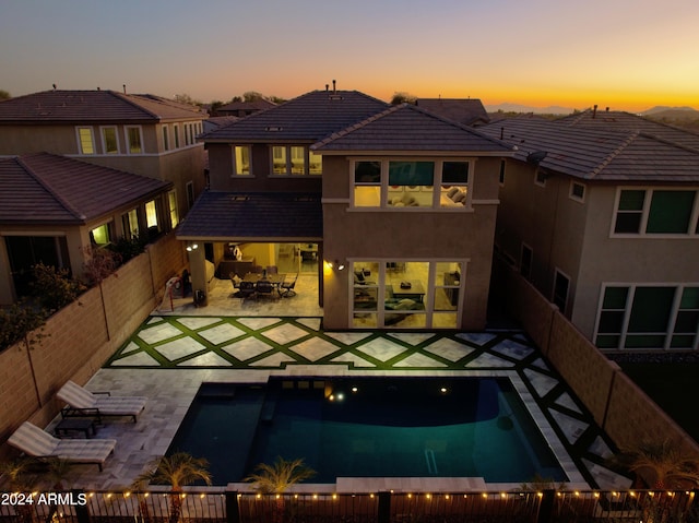 back house at dusk with a patio area and a fenced in pool