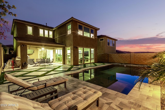 back house at dusk featuring a fenced in pool and a patio area