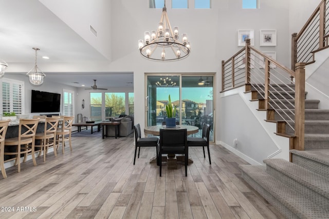 dining room featuring light wood-type flooring, a towering ceiling, and ceiling fan with notable chandelier