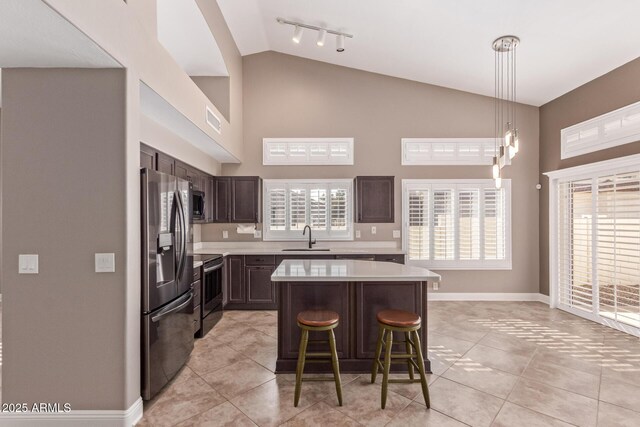 kitchen featuring dark brown cabinetry, light countertops, a kitchen bar, appliances with stainless steel finishes, and a sink
